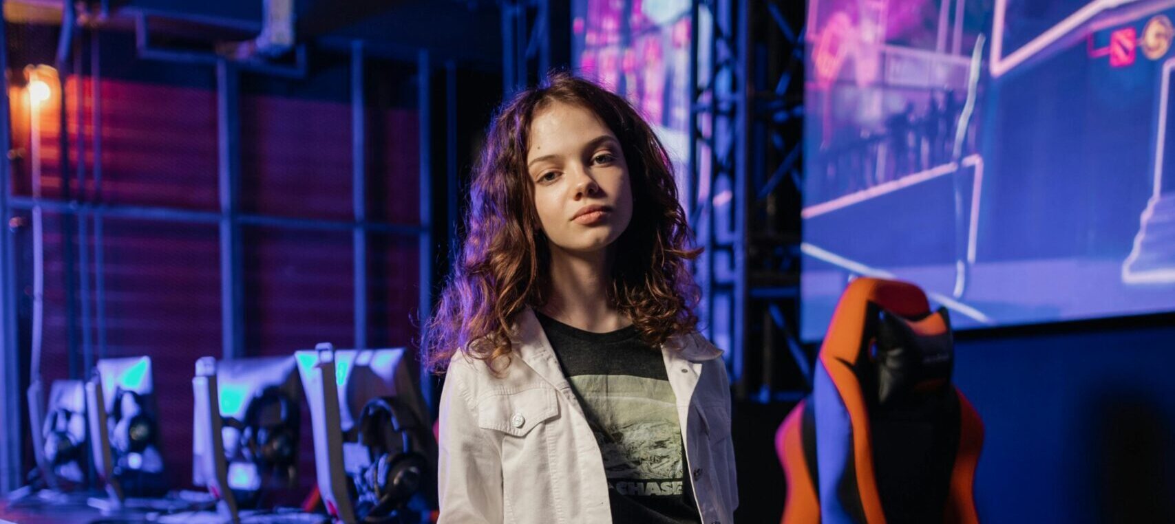 Young woman standing confidently in a modern gaming arena holding a headset.